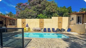 A swimming pool with lounge chairs, a stone patio, and a wooden wall.
