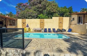 A swimming pool with lounge chairs, a stone patio, and a wooden wall.