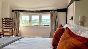 Une chambre à coucher avec un lit, une chaise, une fenêtre avec des rideaux et une lampe sur une table de chevet.