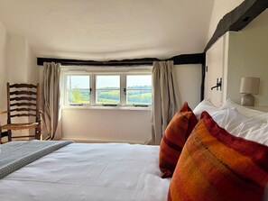 Une chambre Ă coucher avec un lit, une chaise, une fenĂȘtre avec des rideaux et une lampe sur une table de chevet.