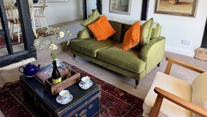 Un salon chaleureux avec un canapé vert, une table basse en bois ornée d’un vase et d’une théière, et un tapis à motifs.