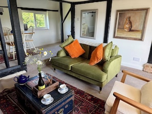 Ein gemütliches Wohnzimmer mit einem grünen Sofa, einem Holztisch mit Vase und Teekanne sowie einem gemusterten Teppich.
