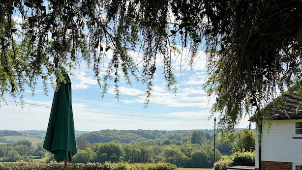 Une terrasse avec une table et des chaises, un parasol vert et une vue sur la campagne.