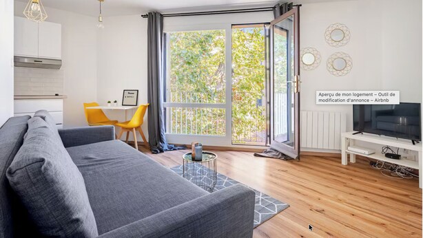 Uma sala de estar moderna com um sofá cinzento, uma mesa de jantar com cadeiras amarelas, um rack para televisão e uma grande porta de vidro deslizante que dá para uma varanda.
