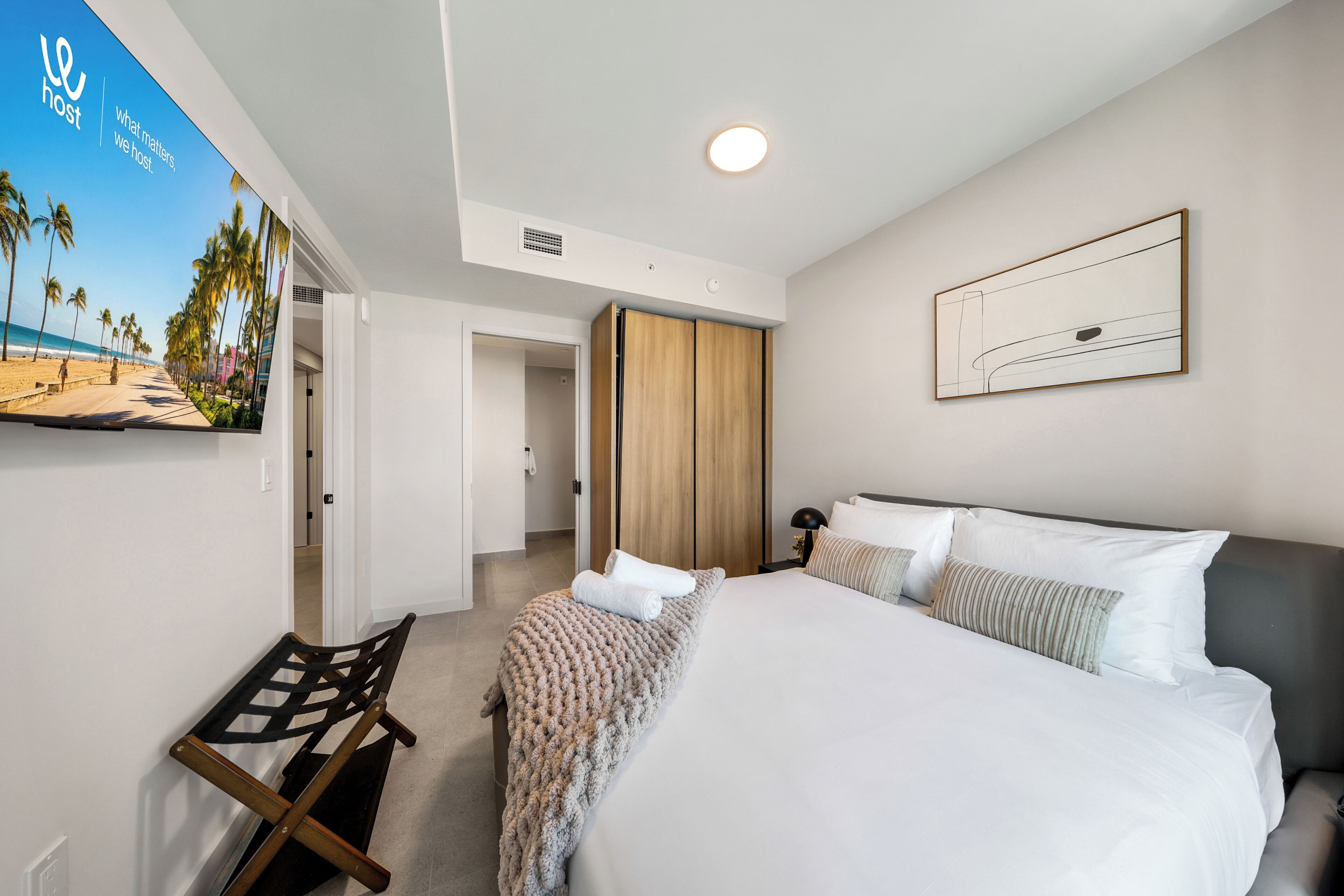 Habitación de hotel con cama, un banco, una obra de arte en la pared y una puerta que da a otra habitación.