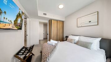Habitación de hotel con cama, un banco, una obra de arte en la pared y una puerta que da a otra habitación.