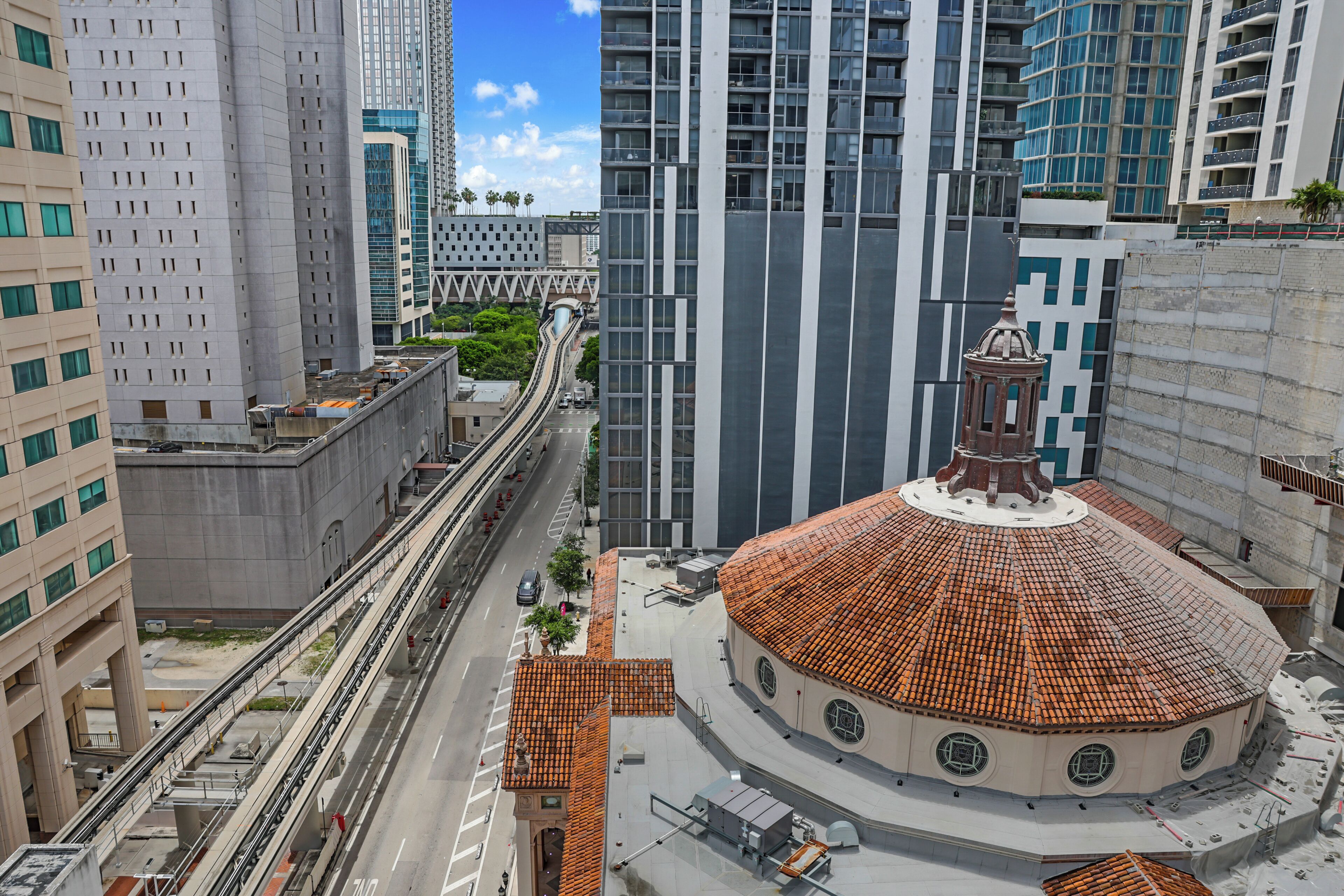 A cityscape with modern high-rise buildings, a circular building with a dome, and a tram line.