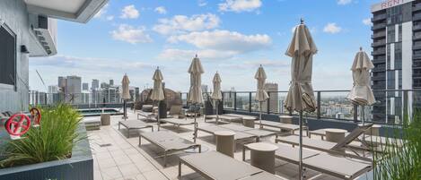 A rooftop terrace with sun loungers, umbrellas, and potted plants.