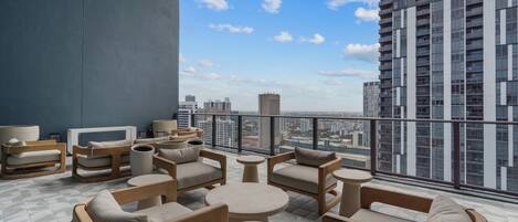 Een dakterras met terrasstoelen, een televisie en uitzicht over de stad.