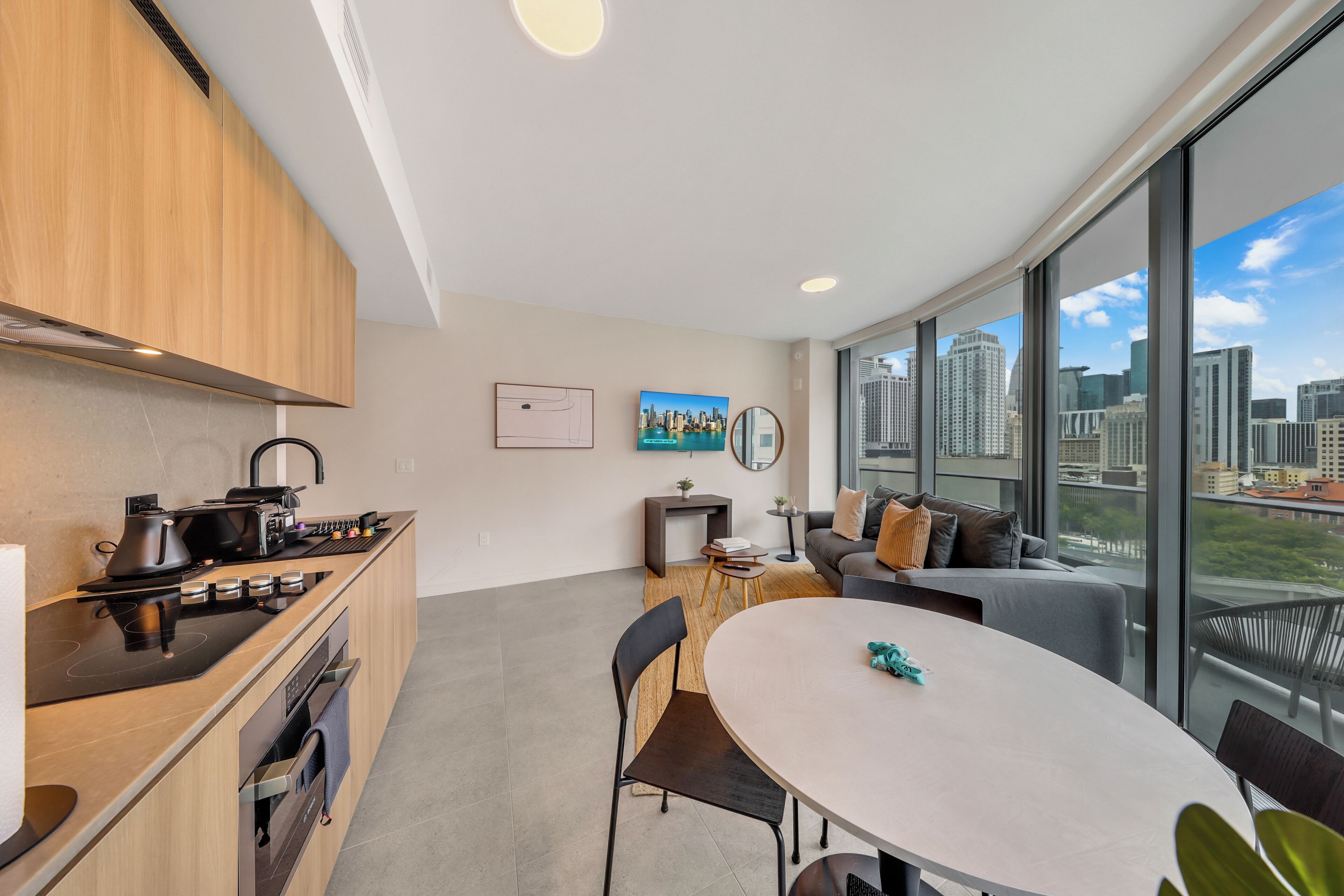 Eine moderne Küche mit Herd, Backofen und Arbeitsplatte, ein Essbereich mit Tisch und Stühlen sowie eine Sitzecke mit Blick auf die Stadt durch große Fenster.