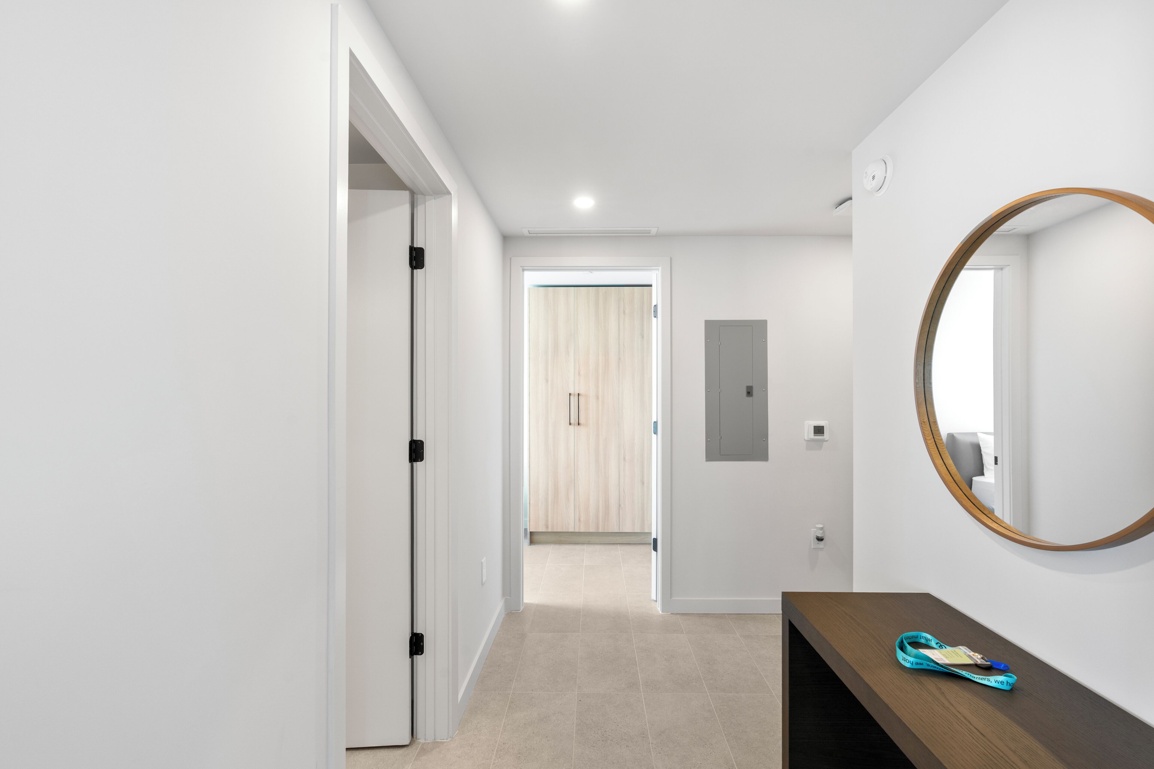 Un couloir avec une porte en bois, un miroir et un banc en bois sur lequel est posée une serviette.