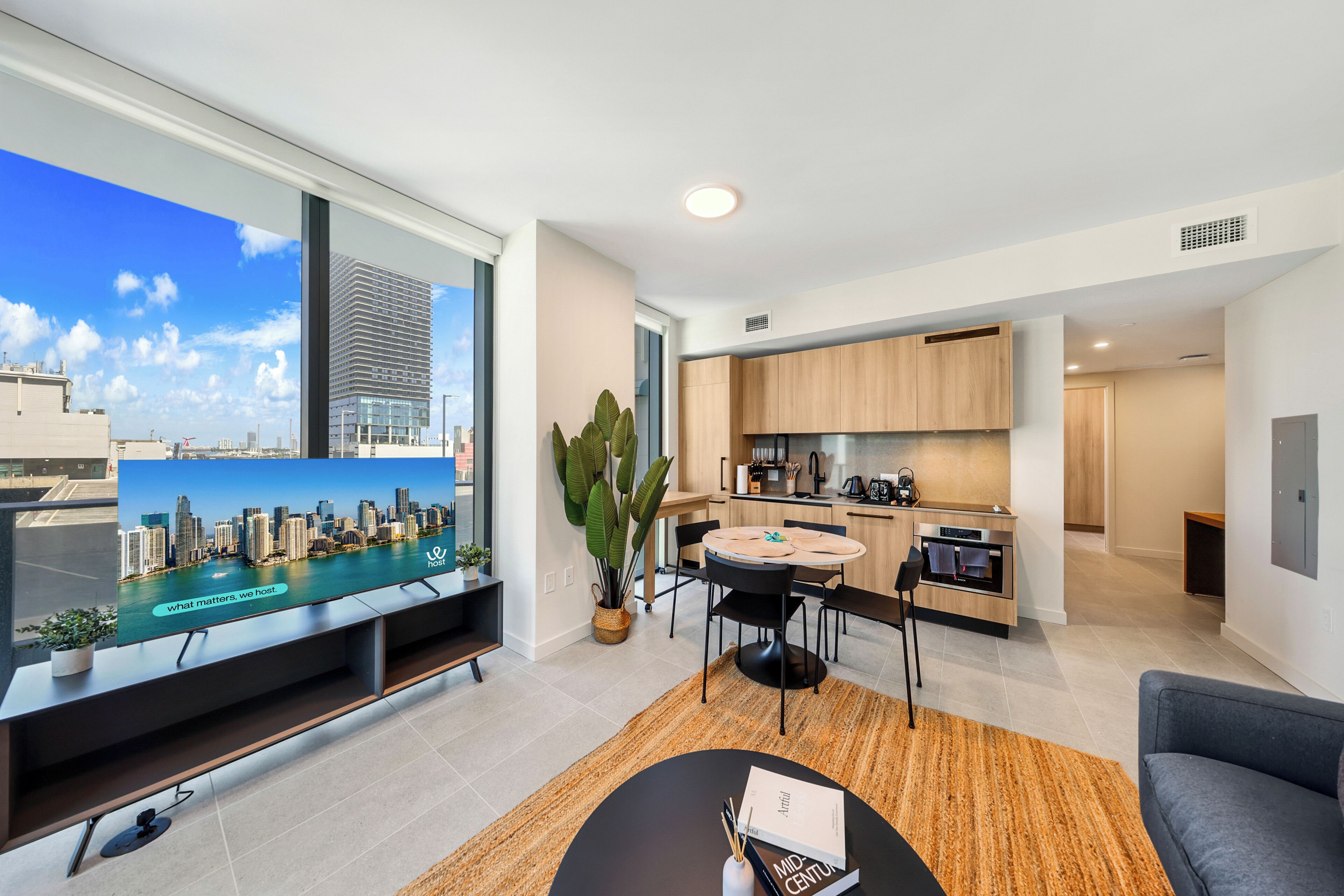 A modern apartment with a city view, a dining area, kitchen, and a living room with a sofa and a coffee table.