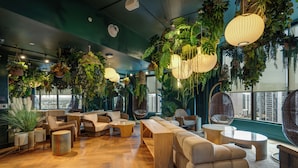 A modern lounge with wooden flooring, comfortable seating, hanging plants, and large windows offering a city view. - Stay Central in Miami - Panoramic views of Biscayne Bay (Miami)