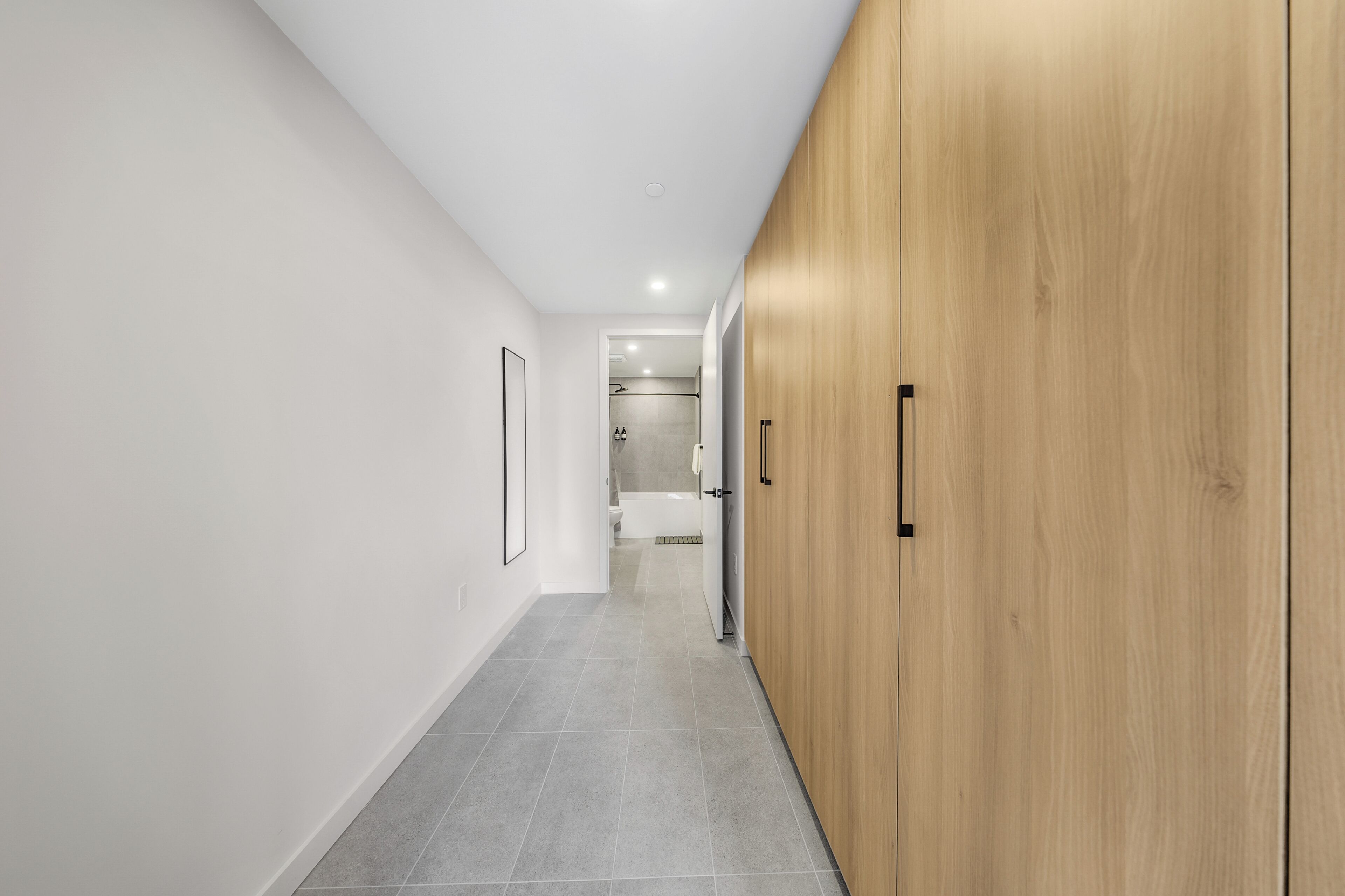 A hallway with a wooden wardrobe, a framed picture, and a tiled floor.