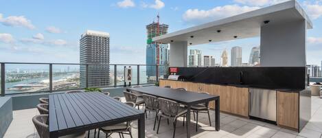 A rooftop terrace with a dining area, kitchen, and city views.