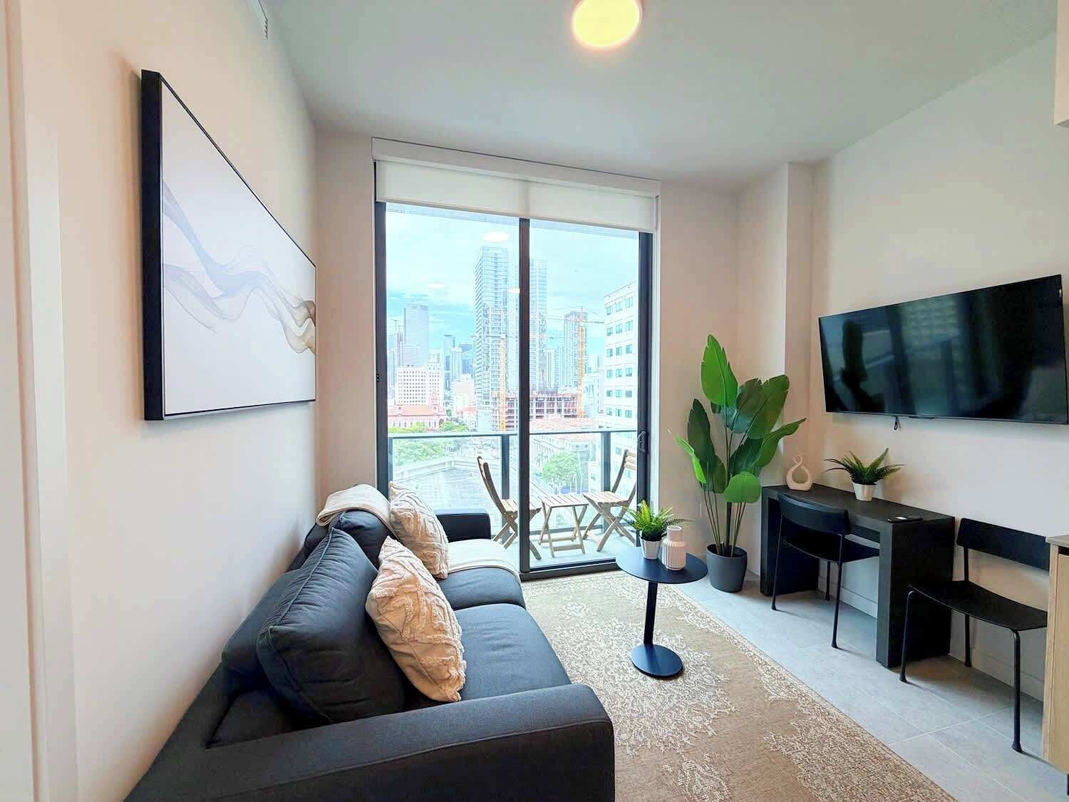 A modern living room with a sofa, a TV, a dining table, and a large window with a city view.