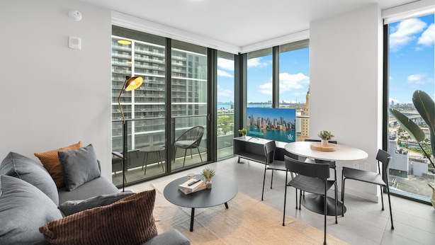A modern living room with a sofa, coffee table, and dining area, large windows with a city view, and a balcony with a railing. - Stay Central in Miami - Panoramic views of Biscayne Bay (Miami)