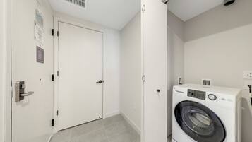 A laundry room with a front-loading washing machine, a closed door, and a vent on the ceiling.