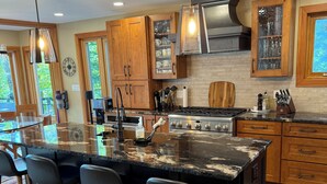 A modern kitchen with wooden cabinets, a large island with bar stools, a stove, and a sink.