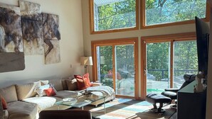 A spacious living area with a high ceiling, large windows, a sofa, a coffee table, and a television.