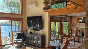 A spacious living area with a large TV, comfortable seating, a fireplace, and a view of the lake.