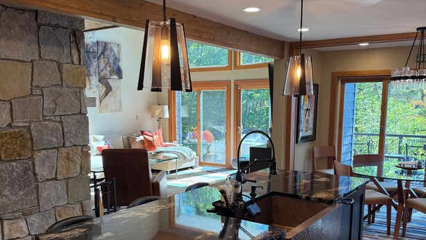 A modern kitchen with a large island, stone wall, and large windows.