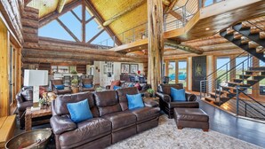 A spacious living area with a high ceiling, wooden beams, a large brown leather sofa, and a staircase. - Luxury Lodge +Guest House + Sleeps 14  + World Cup (Greenwood)