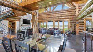 A spacious log cabin interior with a large dining table, comfortable seating, a stone fireplace, and a scenic outdoor view. - Luxury Lodge +Guest House + Sleeps 14  + World Cup (Greenwood)