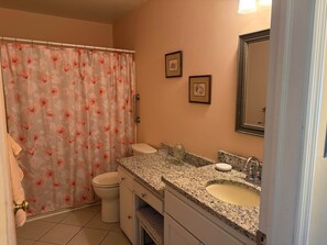 Un baño con cortina de ducha, inodoro, lavabo y dos cuadros enmarcados en la pared.