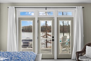 A bedroom with a bed, a chair, and a view of a dock and trees through a sliding glass door. - Fairview Lake Haven | New Waterfront Home | Private Side | 6BR/4BA | Boathouse & Dock (Mineral)