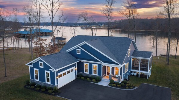 Exterior - A sweeping twilight aerial shows the full front elevation, garage, screened porch, and lit boathouse behind. - Fairview Lake Haven | New Waterfront Home | Private Side | 6BR/4BA | Boathouse & Dock (Mineral)