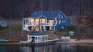 Exterior - From the dock looking toward the house, warm interior light and the covered boathouse reflect on the still water. - Fairview Lake Haven | New Waterfront Home | Private Side | 6BR/4BA | Boathouse & Dock (Mineral)