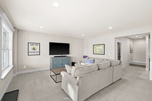 Lower Level Lounge - A comfortable lounge with sofa, TV on a teal credenza, and the game room just beyond. - Fairview Lake Haven | New Waterfront Home | Private Side | 6BR/4BA | Boathouse & Dock (Mineral)