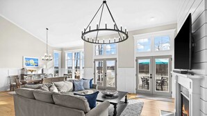 A spacious living room with a fireplace, a large sofa, and a chandelier. - Fairview Lake Haven | New Waterfront Home | Private Side | 6BR/4BA | Boathouse & Dock (Mineral)