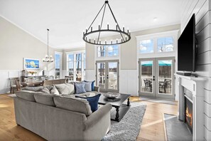 A spacious living room with a fireplace, a large sofa, and a chandelier. - Fairview Lake Haven | New Waterfront Home | Private Side | 6BR/4BA | Boathouse & Dock (Mineral)