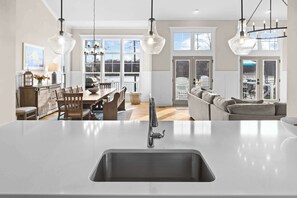 A modern kitchen with a central island, a dining area with wooden chairs, and a living room with a sofa and a view of the outdoors. - Fairview Lake Haven | New Waterfront Home | Private Side | 6BR/4BA | Boathouse & Dock (Mineral)