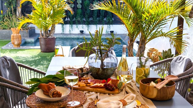 A table set for a meal with various dishes, a bottle of wine, and a view of a pool. - Villa Tharros - Playa del Inglés (Playa del Ingles)