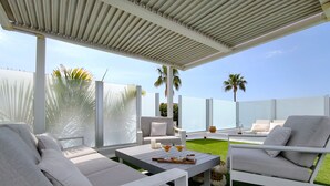 A modern outdoor seating area with white furniture, a small table with drinks, and a view of the ocean. - Villa Tharros - Playa del Inglés (Playa del Ingles)