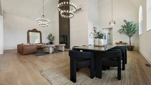 Een moderne woonkamer met een grote spiegel, een bank, een eettafel met stoelen en een kroonluchter.