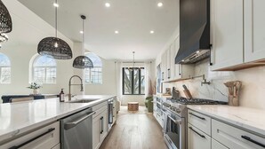 Een moderne keuken met een centraal eiland, roestvrijstalen apparatuur en hangende lampen.