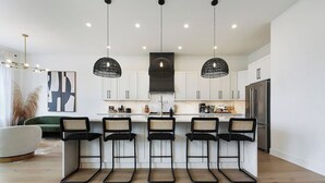 Een moderne keuken met witte kasten, een centraal eiland met barkrukken en hanglampen.