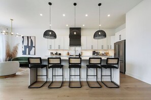 A modern kitchen with white cabinets, a central island with bar stools, and pendant lighting. - Converted Church Escape | Sleeps 16 | Views (Pittsburgh)