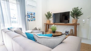 A modern living room with a large sofa, a flat-screen TV on a wooden stand, and two potted plants. - Modern central apartment for couples with 2 balconies - relax in style (Rodos)