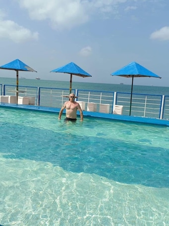 A man in a swimming pool with clear water, blue umbrellas, and a railing.. Beautiful mansion available, pet friendly