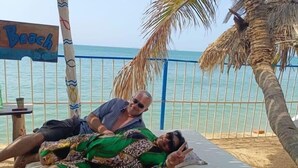 En plats vid stranden med en träkonstruktion, palmer och en skylt med texten ”Strand”.