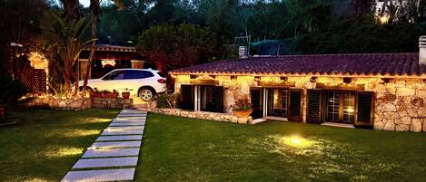 A stone house with a tiled roof, a paved driveway, and a parked car.