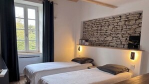 Ett rum med två sängar, en stenmur, en hylla med böcker och ett fönster med gardiner.