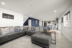 Ein modernes Wohnzimmer mit einer Eckcouch, einem kleinen Tisch und einer Küche im Hintergrund.
