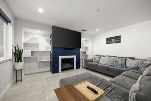 Ein modernes Wohnzimmer mit Kamin, grauem Sofa und Flachbildfernseher.