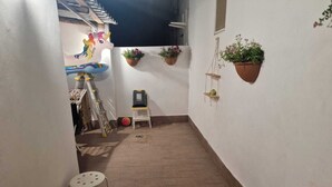 A narrow corridor with a tiled floor, a white chair, a ladder, and hanging planters with flowers. - Maty's House 2 steps from the sea (40 mt) (Reggio Calabria)